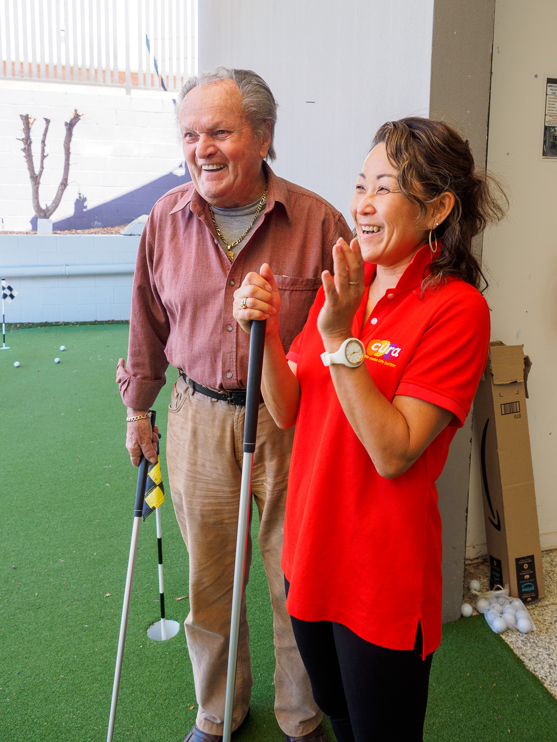 Cura team member and older man smiling during a putting activity